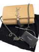 Beige handbag with chain detail and tassel on a black Saint Laurent bag