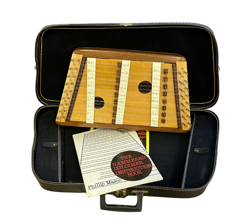 Wooden hammered dulcimer in a black case with an instruction book on a white background