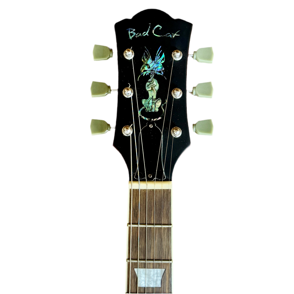 Bad Cat Instruments Les Paul Style Electric Guitar headstock with 'Bad Cat' branding and decorative elements on a white background