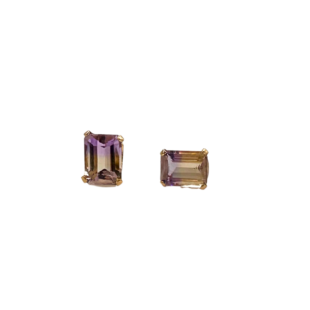 Two emerald-cut gemstones in gold settings on a white background