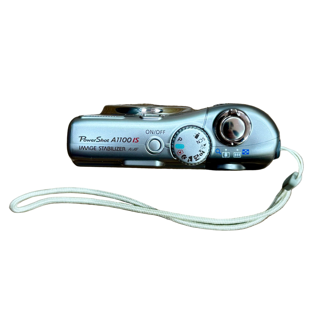 Canon PowerShot A1100 IS 12.1 MP Digital Camera w/ Case - Silver Digital camera with a lanyard on a white background