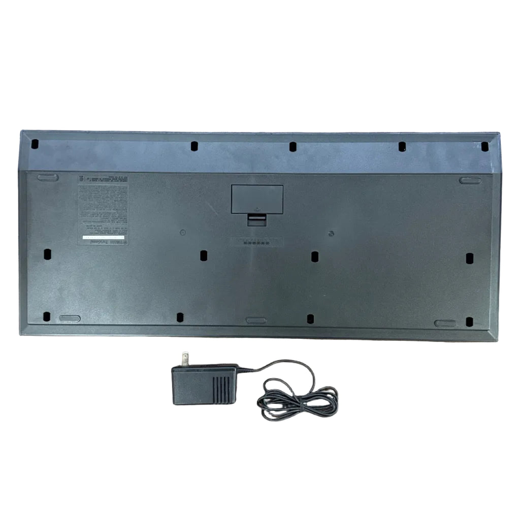 Yamaha PortaSound PSS-470 49-Key Digital Synthesizer Keyboard Back view of a black electronic device with a power adapter on a white background