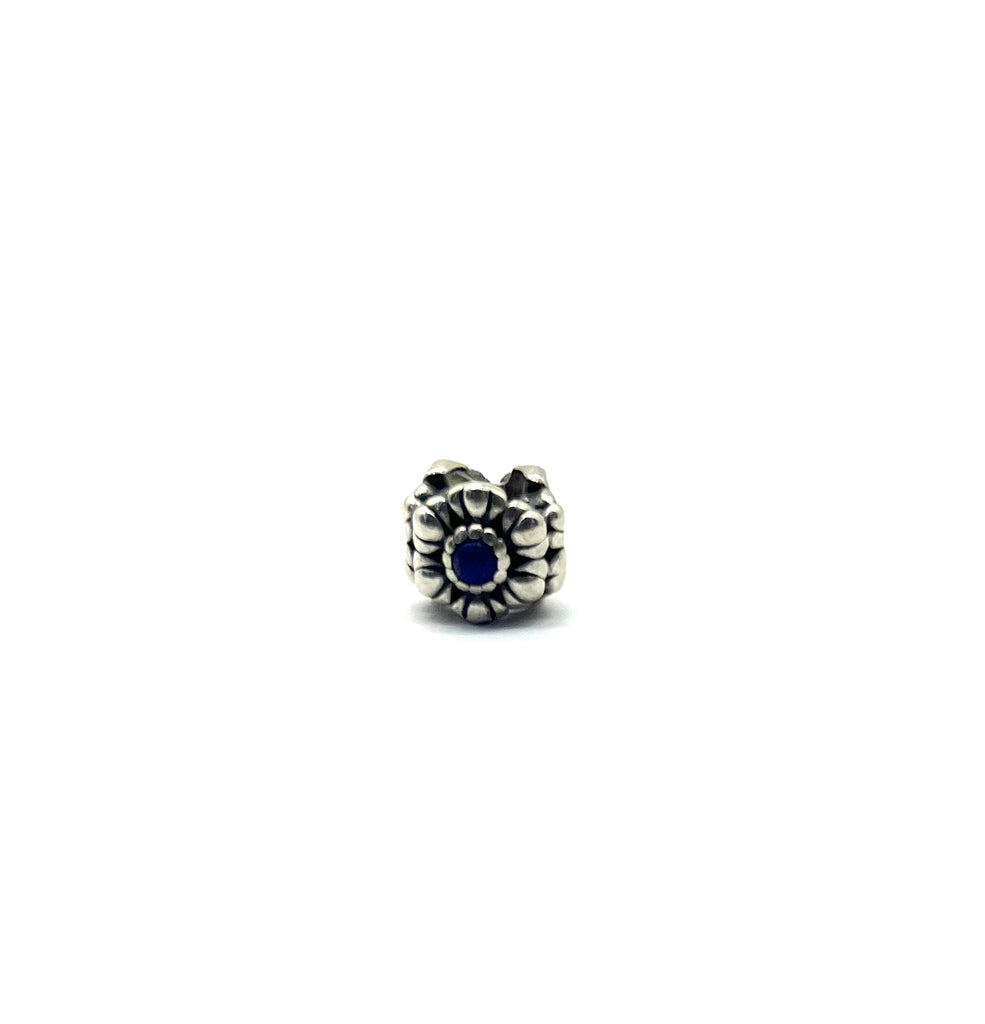 Silver charm with a blue gemstone on a white background