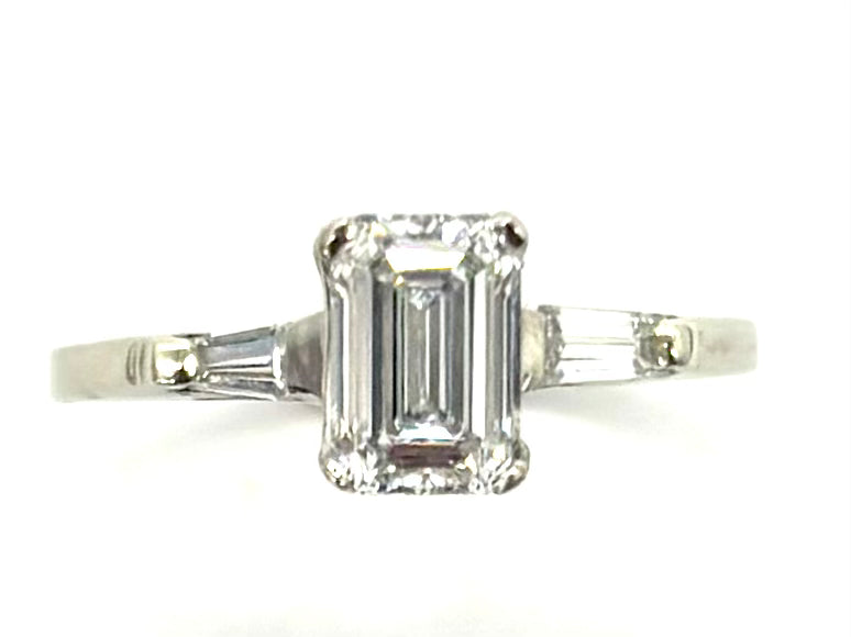 Diamond ring with emerald-cut center stone on a white background