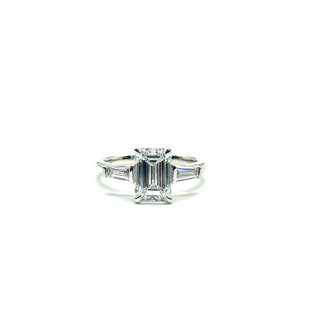 Diamond ring with emerald-cut center stone and baguette side stones on a white background