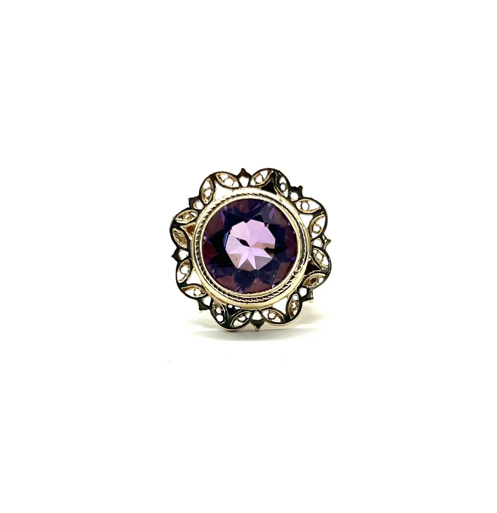 Jewelry ring with purple gemstone and gold-tone setting on a white background