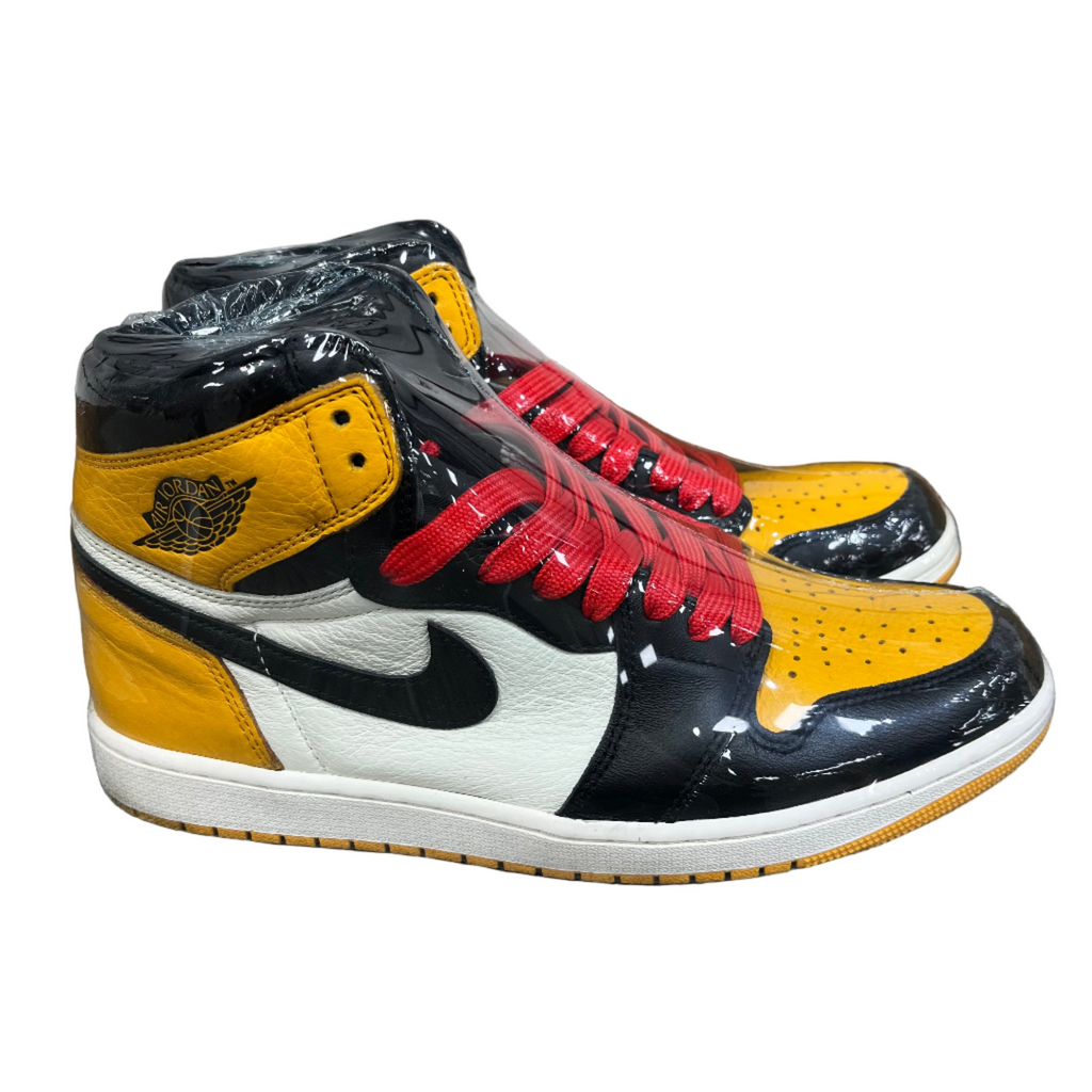 Black, yellow, and red high-top sneakers on a concrete floor with a white wall in the background.