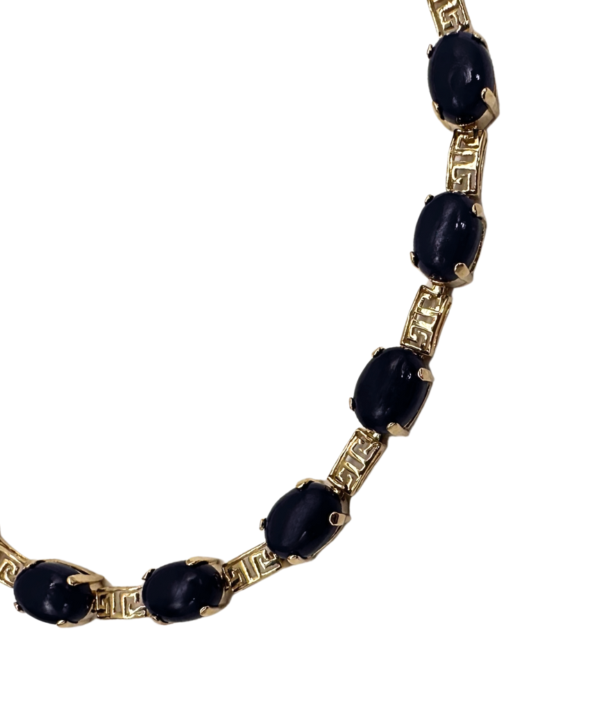 Gold necklace with black gemstones on a white background